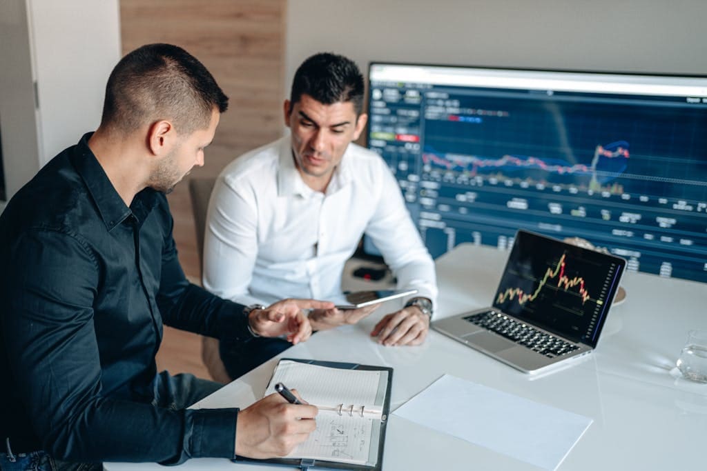 Two businessmen analyzing financial data on digital screens during a collaborative meeting.