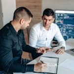 Two businessmen analyzing financial data on digital screens during a collaborative meeting.