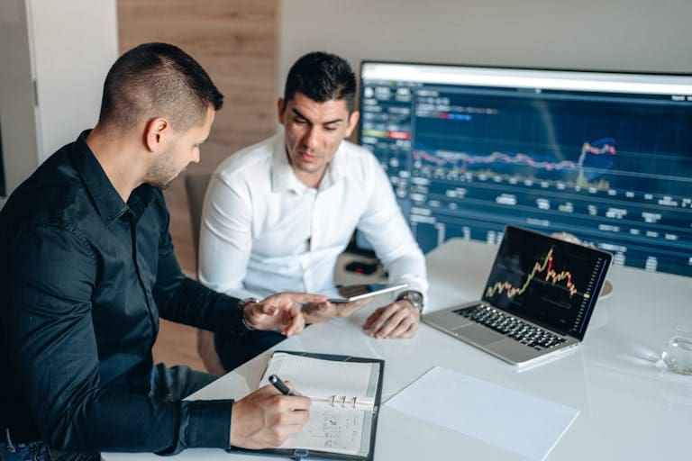 Two businessmen analyzing financial data on digital screens during a collaborative meeting.